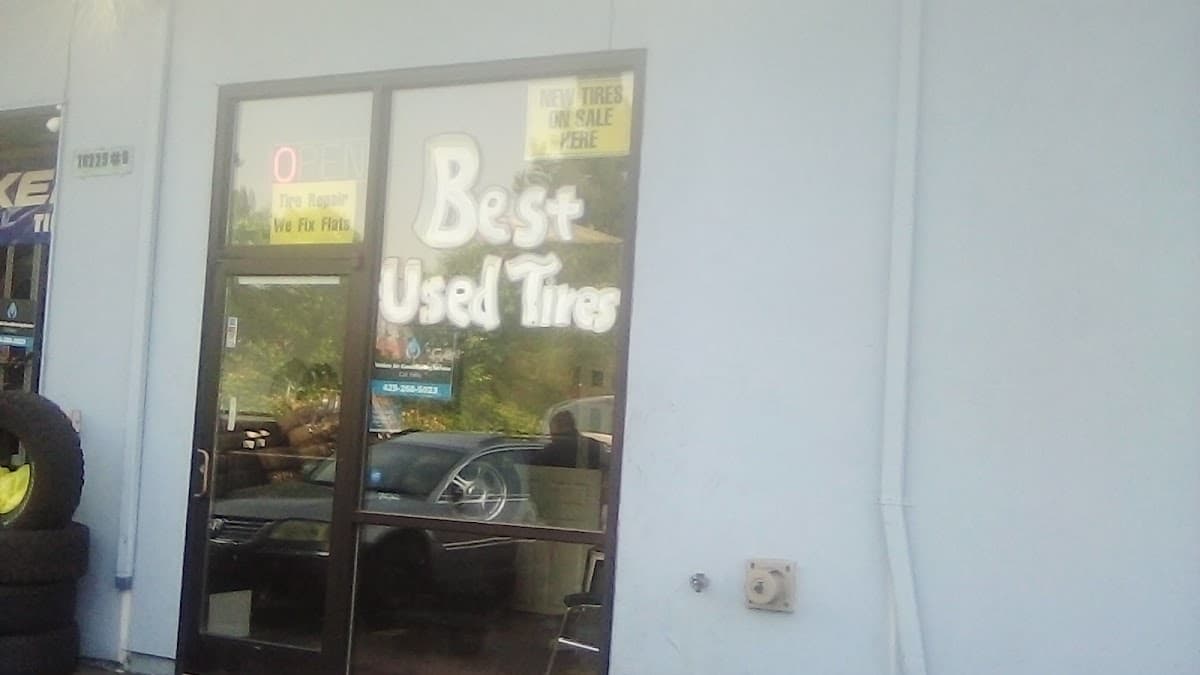 The shop's glass door with "Best Used Tires" hand-painted on the window and an "OPEN · Tire Repair · We Fix Flats" decal, tires stacked beside it.
